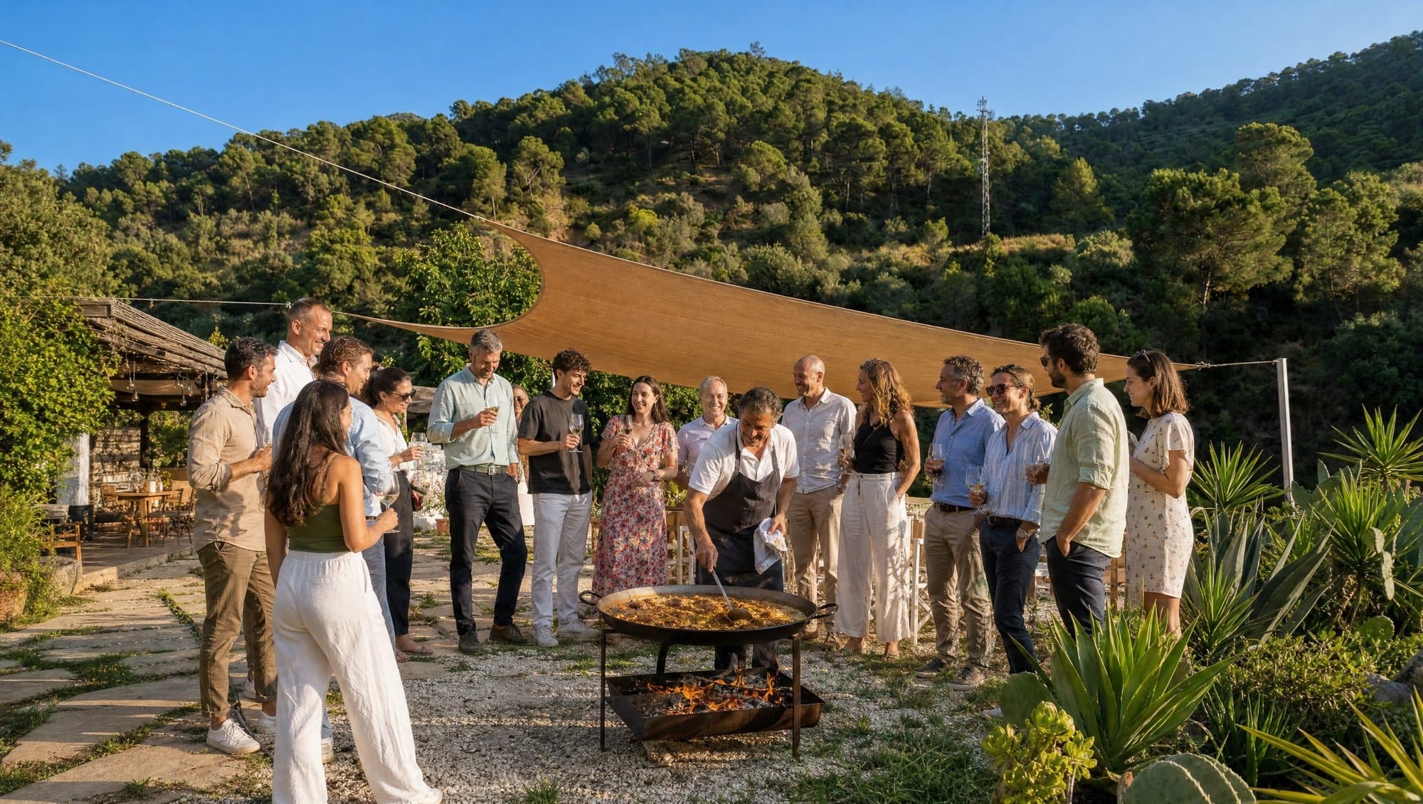 A corporate team gathered around a paella cooking over a wood fire on a finca terrace in the hills above Marbella