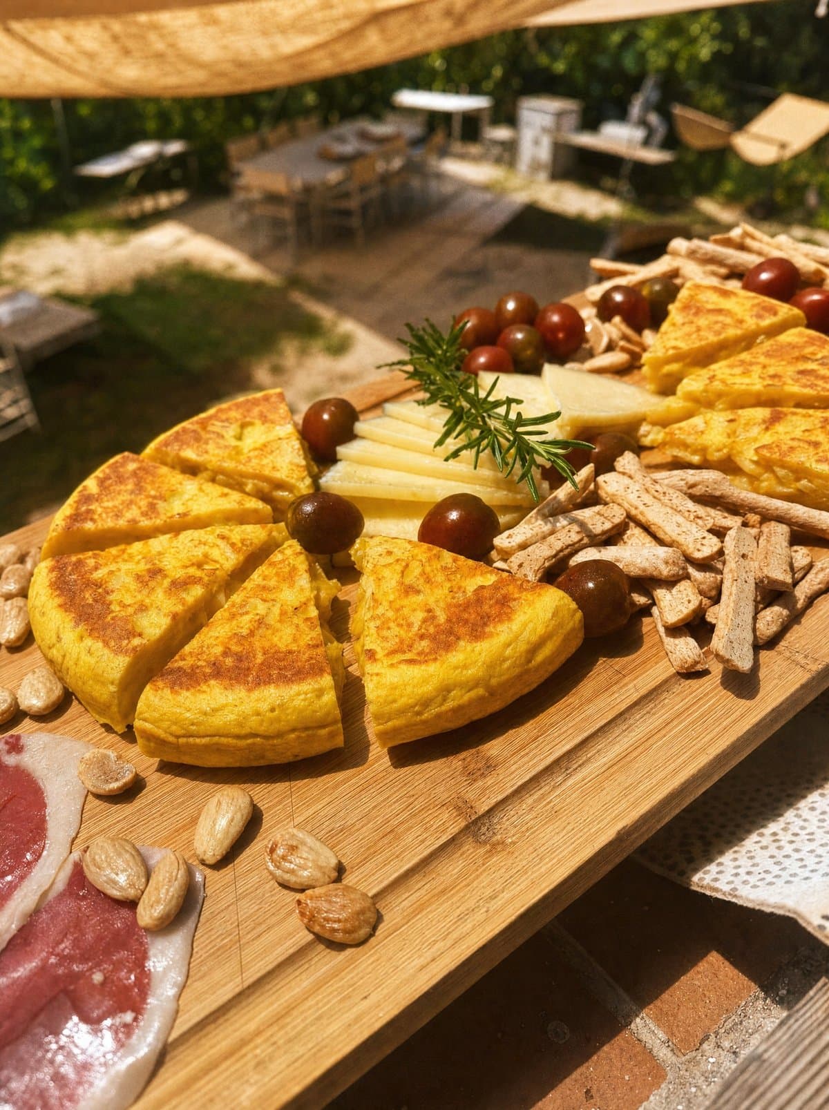 Tapas board at the finca in Ojén — Spanish tortilla, cheese, cherry tomatoes, almonds and jamón under the shade sails before the paella cooking class
