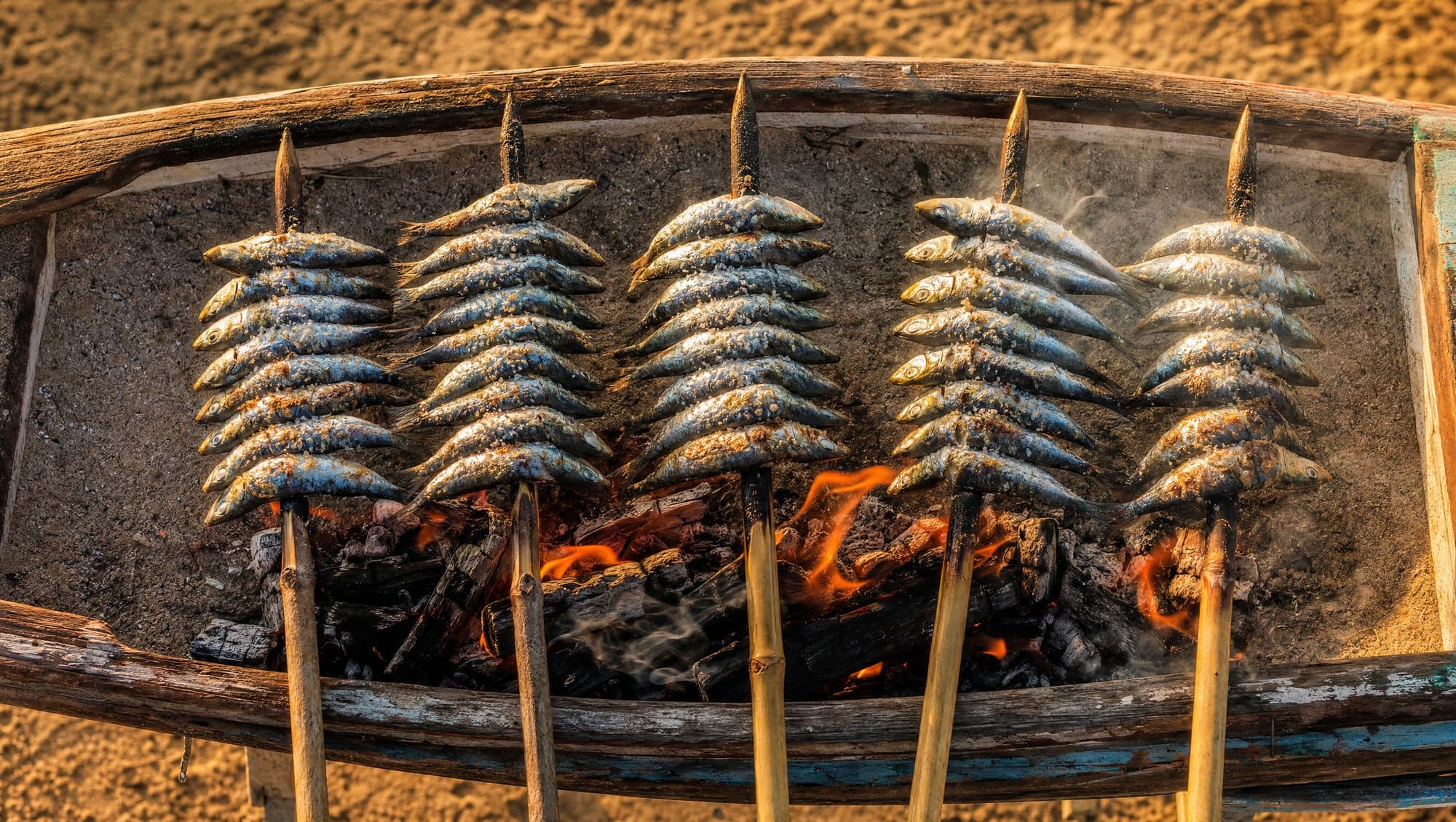 Espetos de sardinas grilling over olive wood embers in a beach barca on the Marbella coast at sunset